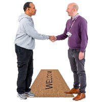 Two people shaking hands over a Welcome mat