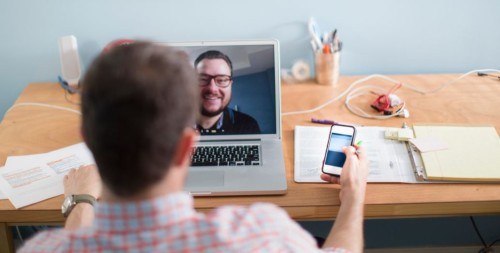 Two men chatting to each other - one at a desk, one on a laptop