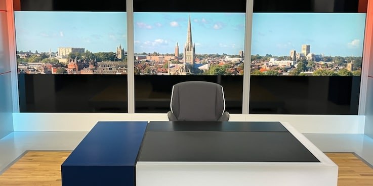 TV news studio with Norwich skyline behind, centred on the steeple of Norwich Cathedral
