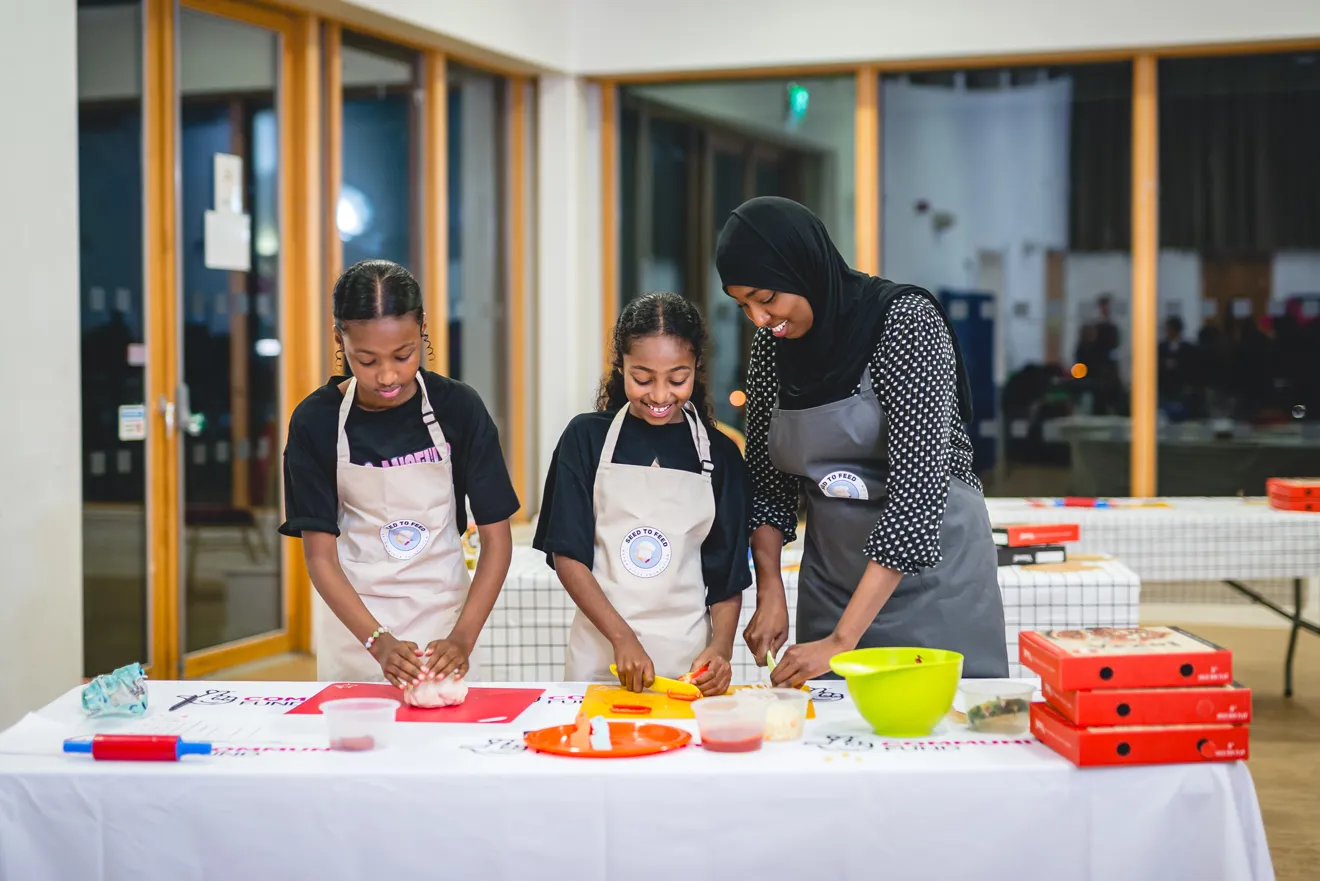 A young woman and two girls prepare ingredients for cooking. They are smiling.