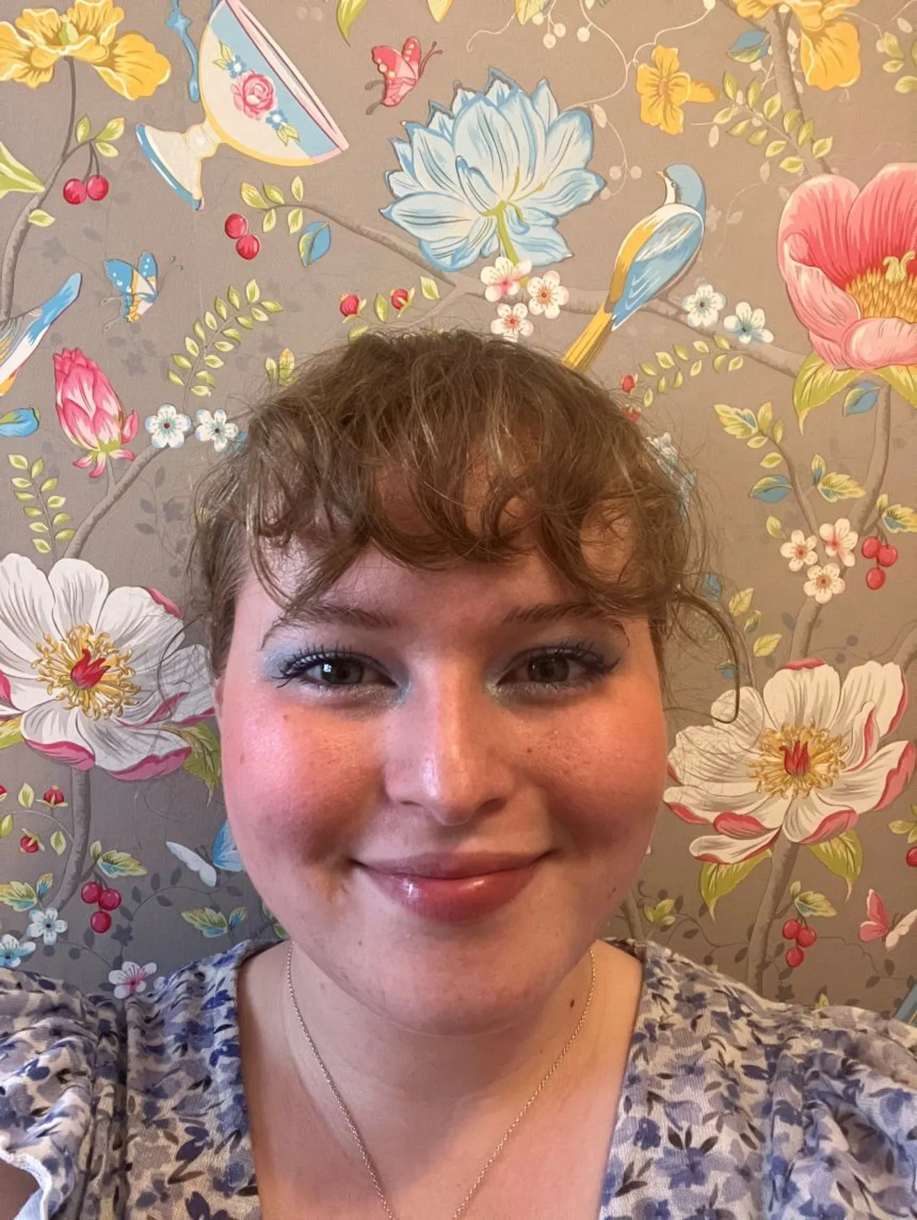Llun o Niamh mewn top blodeuog o flaen papur wal blodeuog