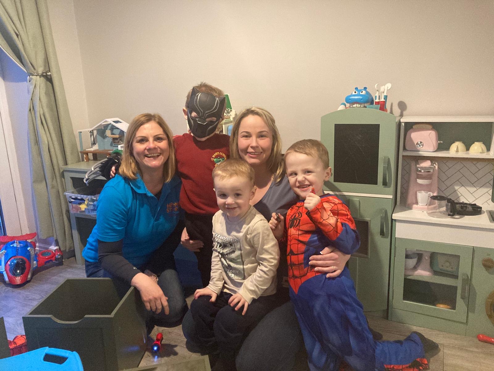 Two people with three children together smiling in a room surrounded by toys.