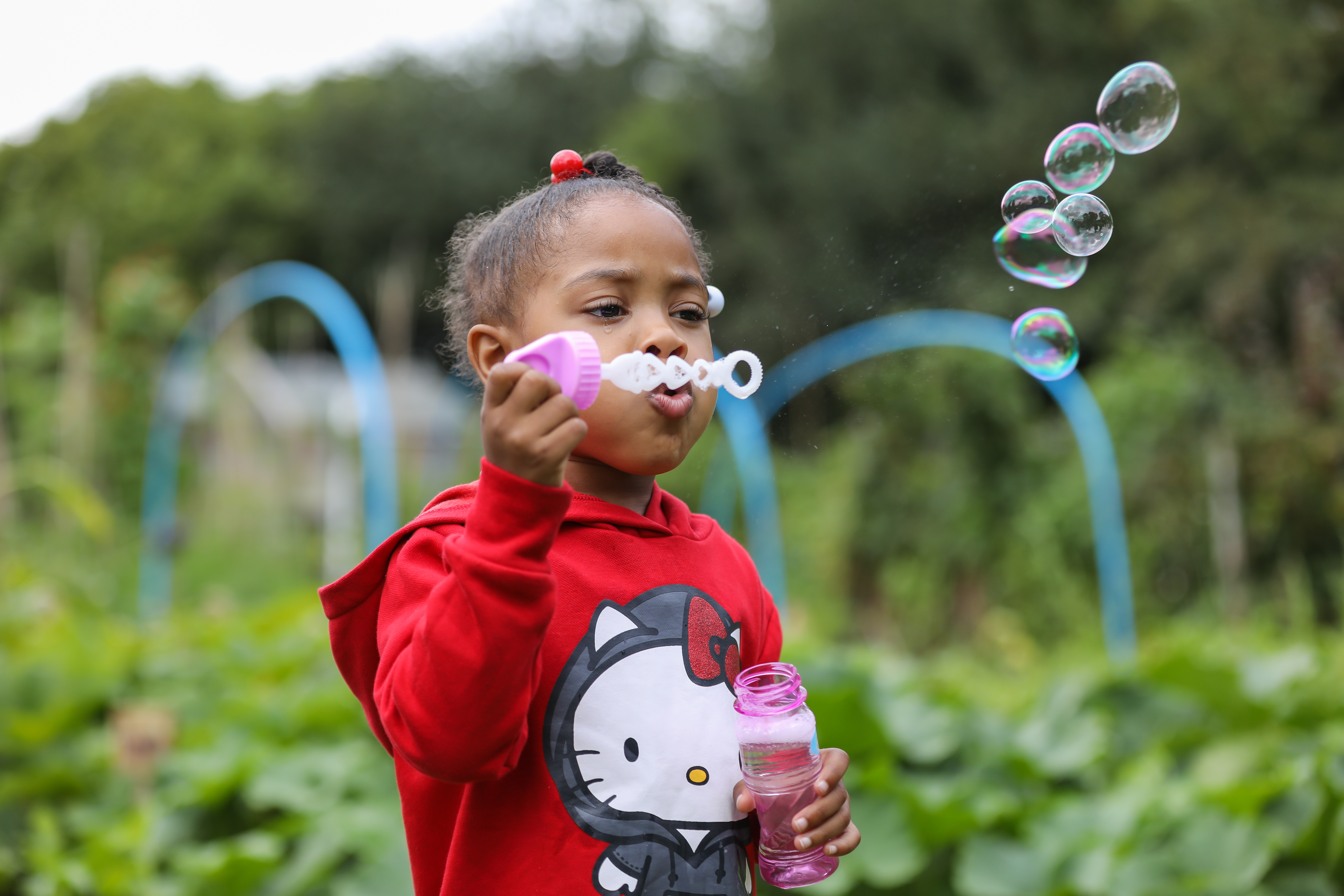 A young girl standing outside blows bubbles. 