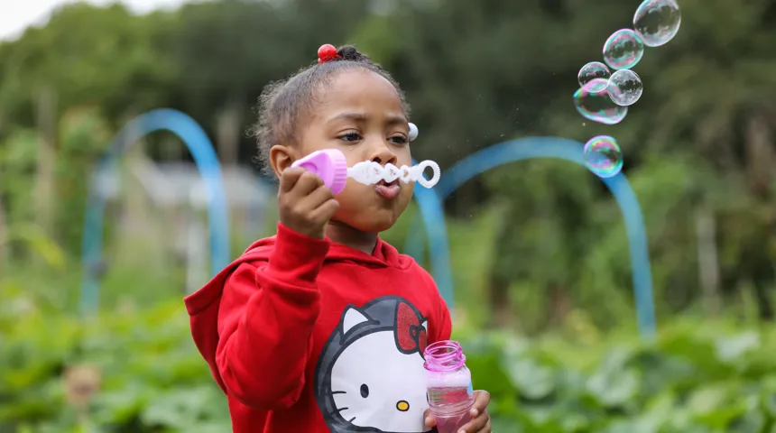A young girl standing outside blows bubbles.