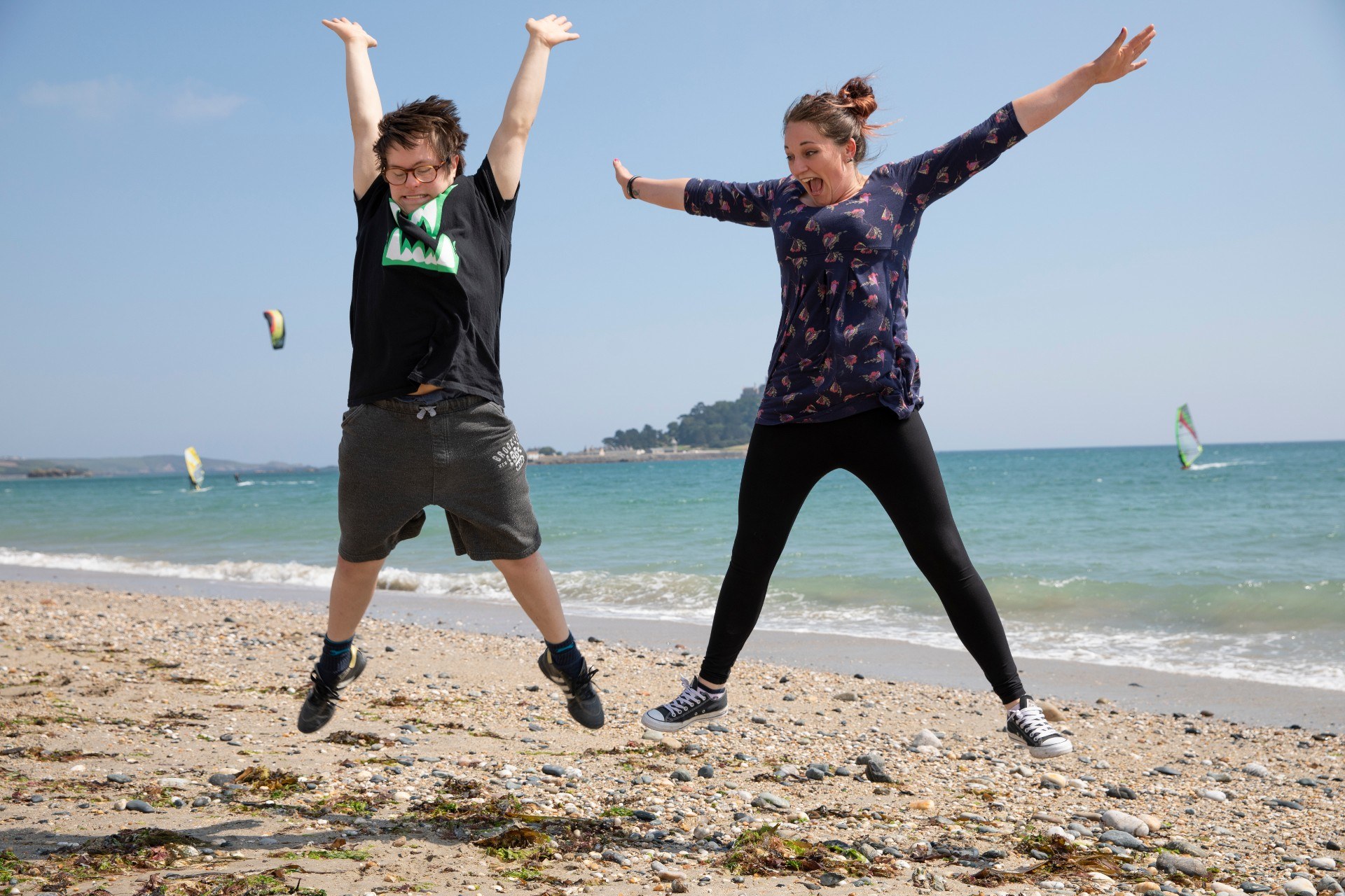 Mencap participant and support worker jumping in the air on a beach