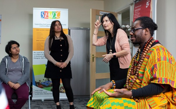 Four people in a group discussion, one person is signing to others in the room.