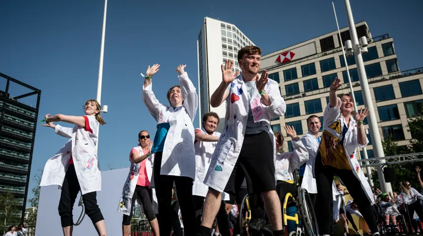 A dance group perform on stage, outside, at a dance festival. They are smiling.